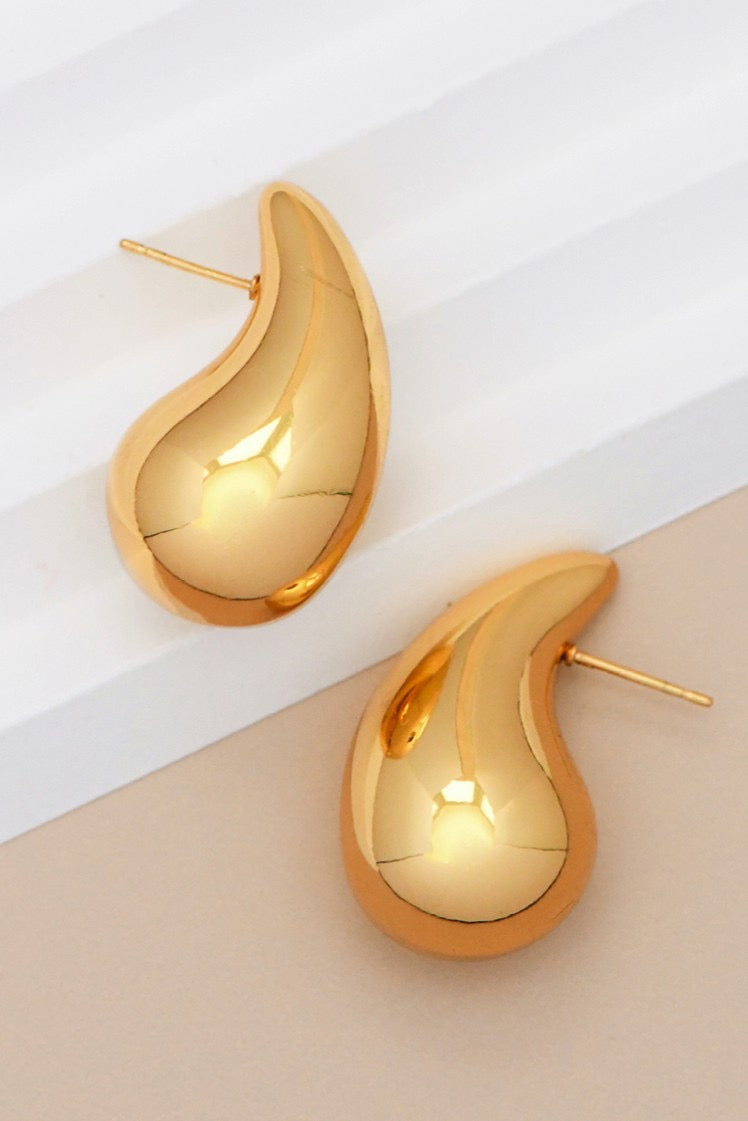 Gold teardrop earrings on a white and beige background