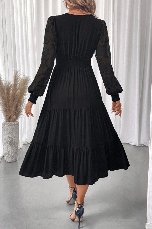 Black dress with sheer sleeves worn by a person in a minimalistic setting