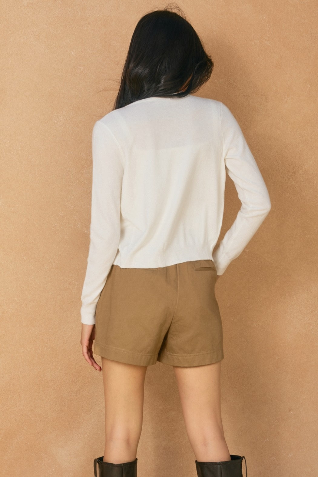 Person wearing a white sweater and brown shorts against a beige background
