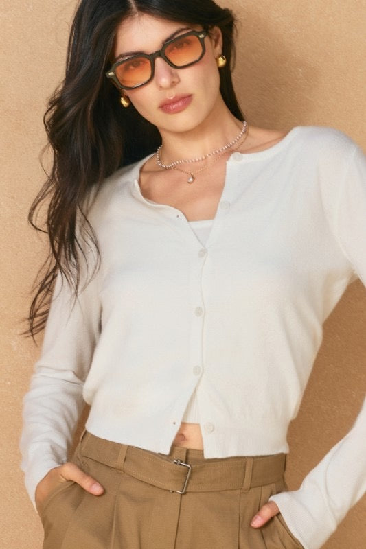 Woman wearing a white cardigan and brown pants against a beige background