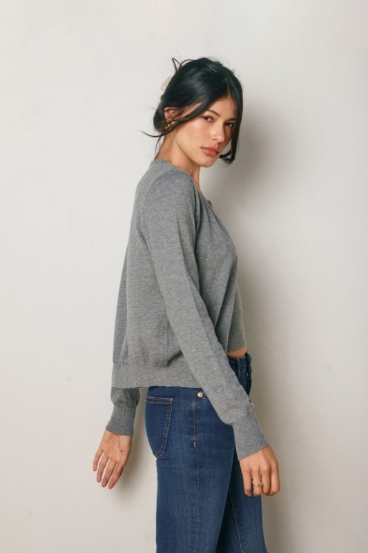 Woman wearing a gray sweater and blue jeans against a plain background