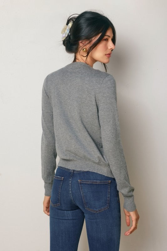 Woman wearing a gray sweater and blue jeans against a plain background