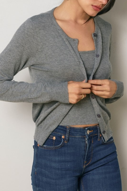Person wearing a gray cardigan and blue jeans against a white background