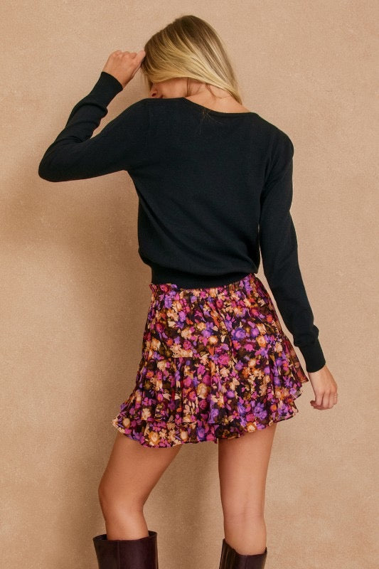 Person wearing a black long-sleeve top and floral skirt against a beige background