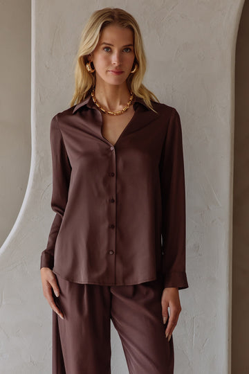Woman wearing a brown satin shirt and pants set against a neutral wall.